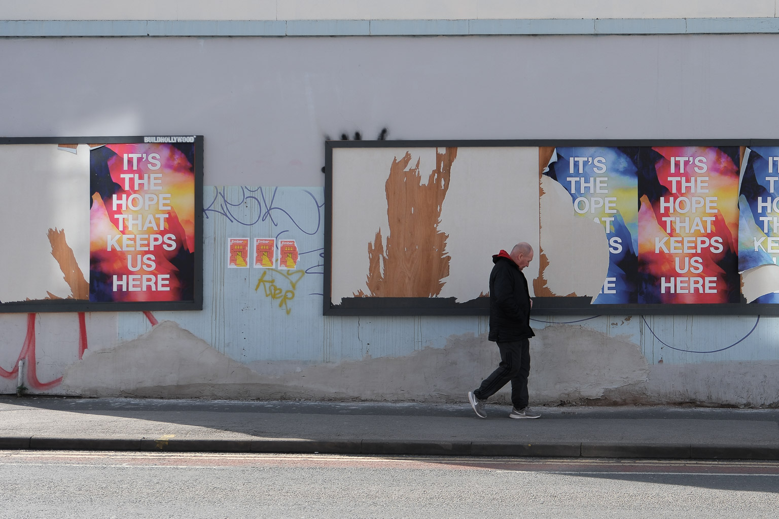A man walking past billboard posters on a side Street in Sheffield